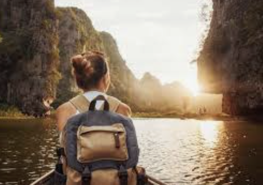 A woman in a boat on a river at sunset, surrounded by tall cliffs.