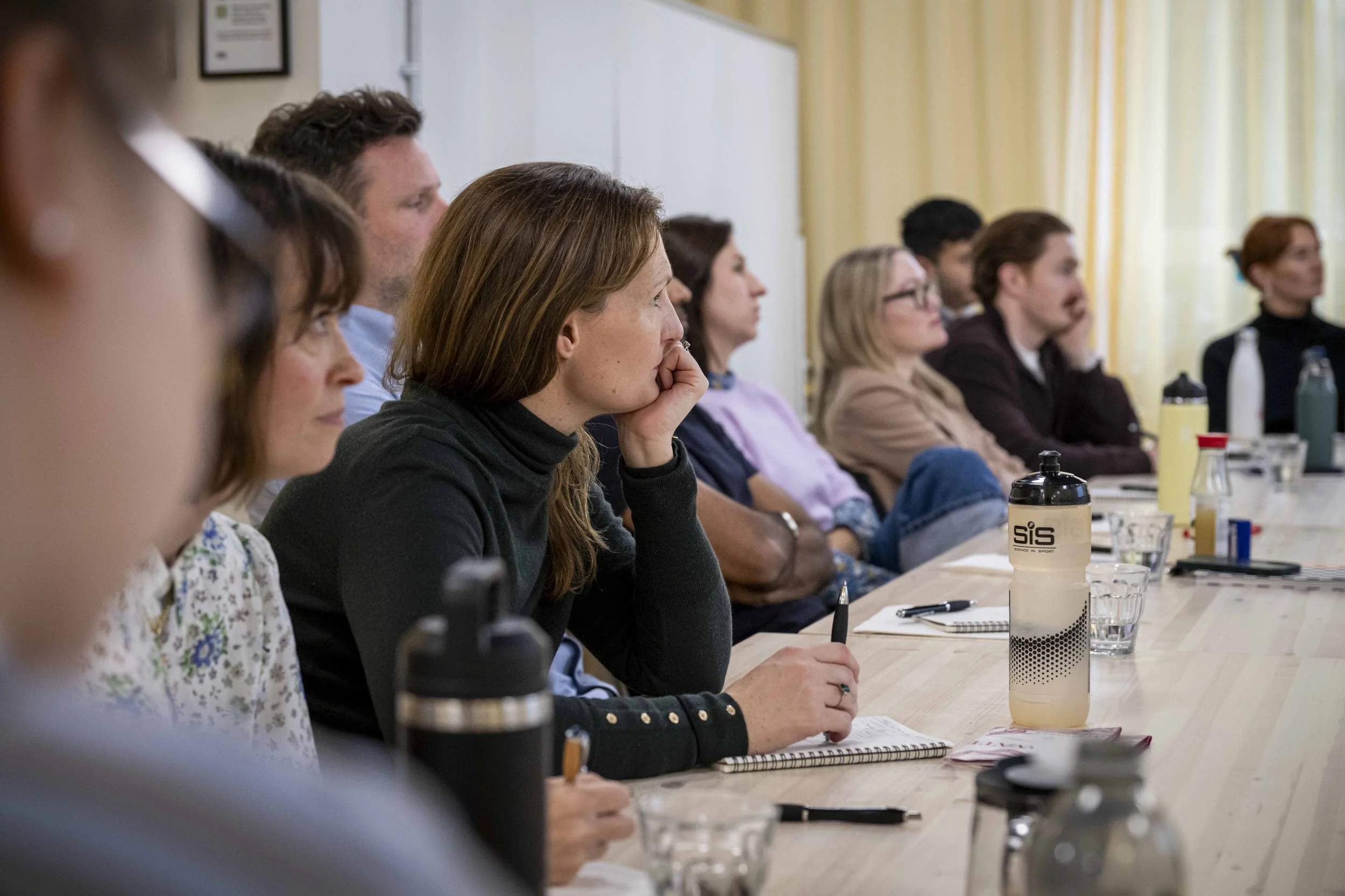 People seated around a table during a GIEM Experience Marketing Masterclasses, listening attentively and taking notes.
