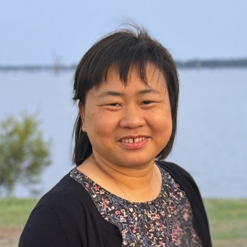 A woman standing outdoors near a body of water, smiling.