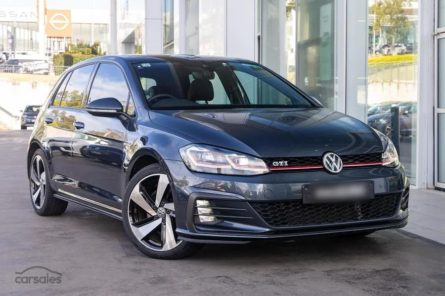 Dark gray Volkswagen Golf GTI parked outside a modern building with glass walls.
