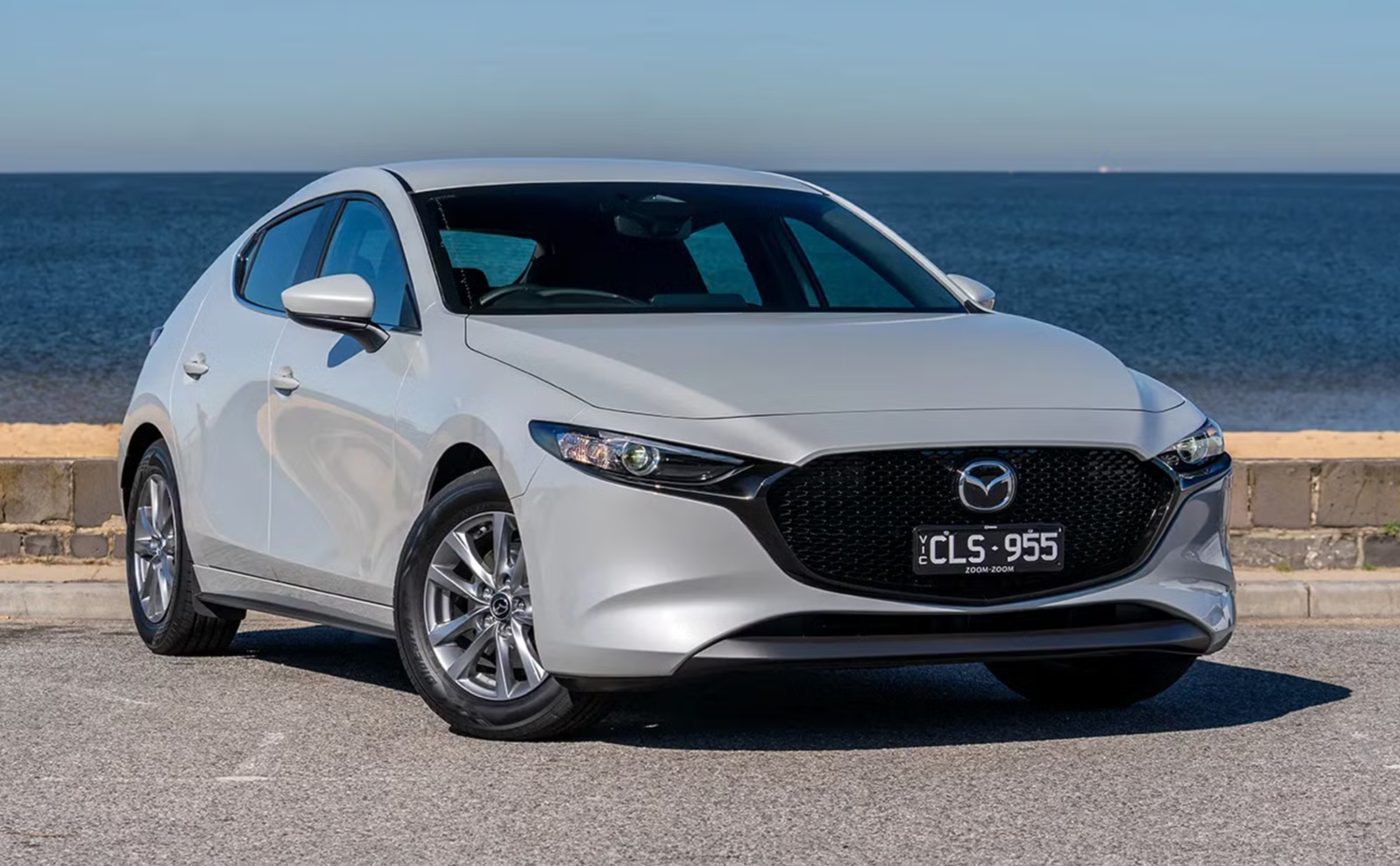 Gray Mazda sedan parked near the ocean on a street with a brick barrier
