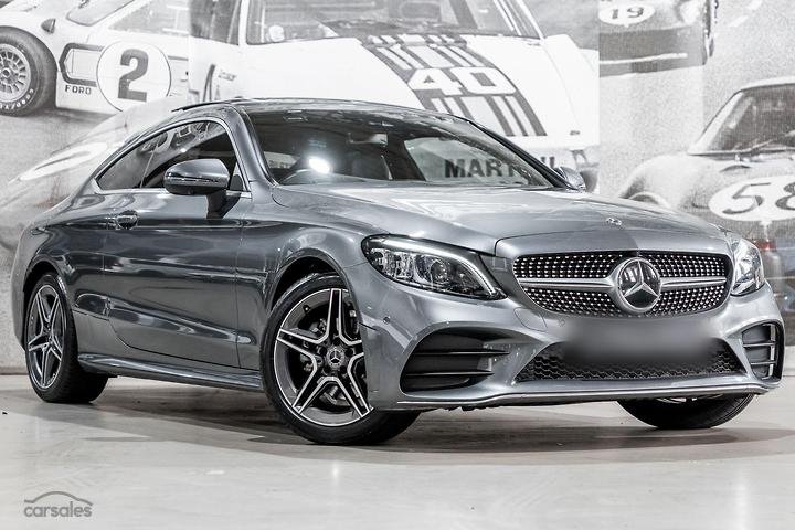 Silver Mercedes-Benz coupe in an indoor showroom with black and white vintage car posters in the background.