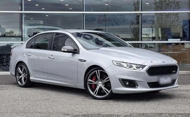 White sedan parked outside a building with glass windows and a sidewalk in the background.
