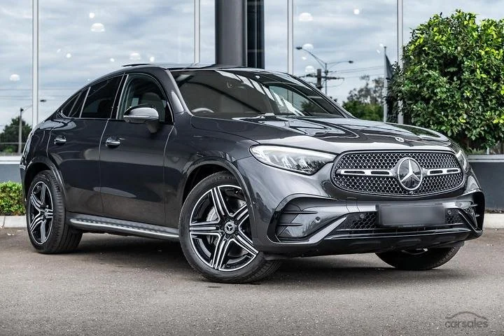 Black Mercedes-Benz hatchback parked outdoors near a green shrub, with a city view in the background.