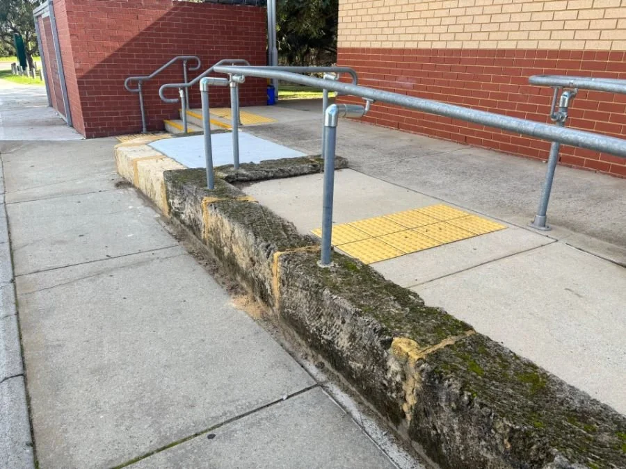 Sidewalk with a wheelchair ramp and yellow tactile paving near a brick building with a sidewalk curb.