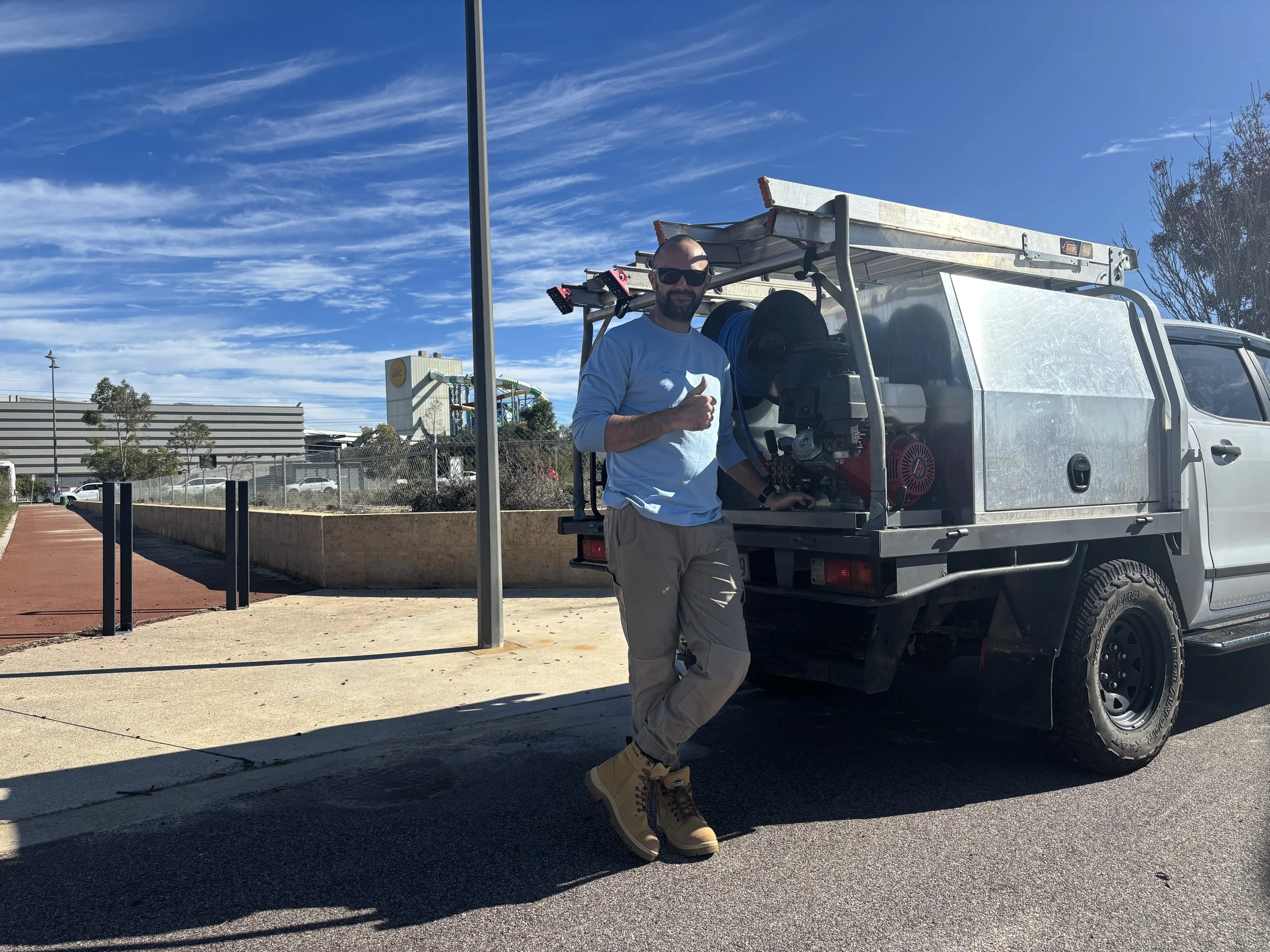 Man standing next to a utility truck with equipment, giving thumbs up on a sunny day.