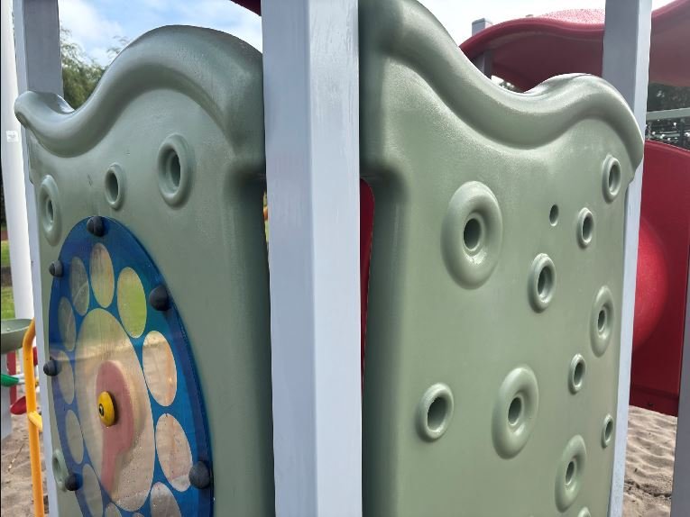 Close-up of a playground climbing structure with various circular and indent features, set outdoors in a park or playground area.
