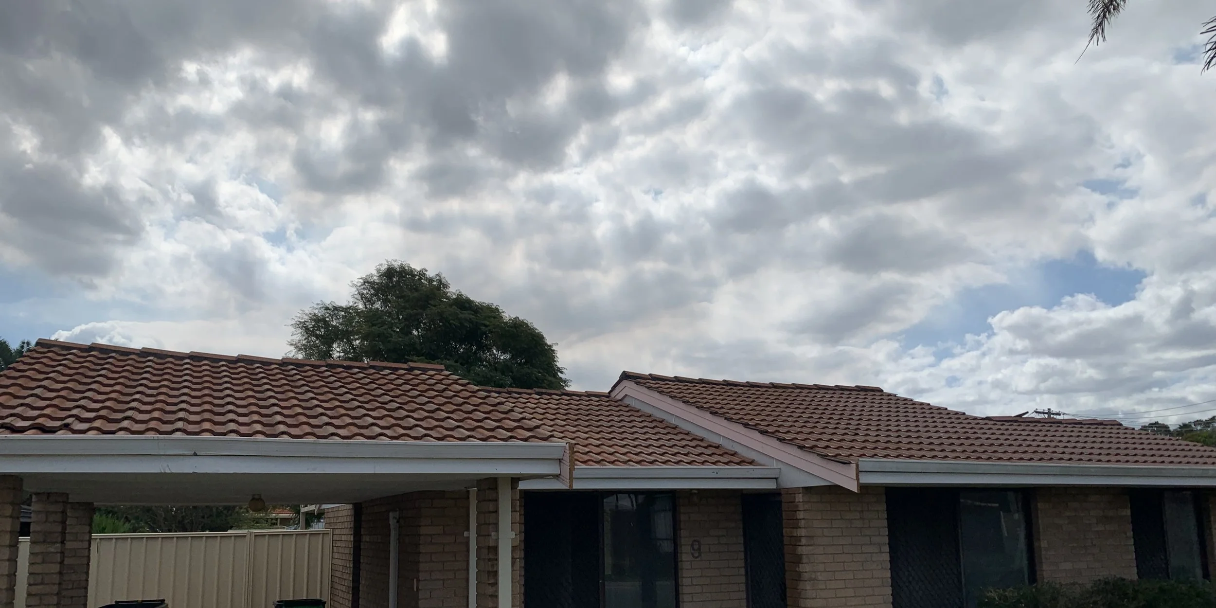 Residential house with red tile roof, brick walls, and a cloudy sky overhead.