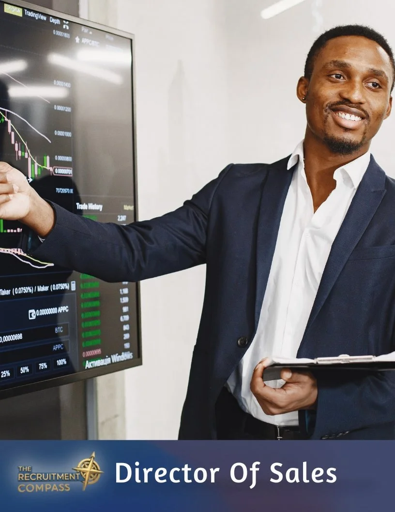 A man in a business suit presenting data on a large screen displaying a financial chart with candlesticks and trade history. He is smiling and holding a tablet. The caption at the bottom reads "Director Of Sales" with a logo for "The Recruitment Compass."