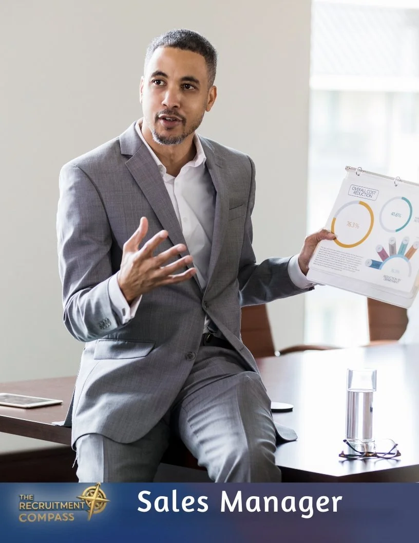 A man in a grey suit holding a presentation board, seated on a conference table in a modern office.