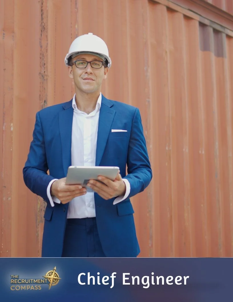 A man in a blue suit and white shirt wearing glasses and a white safety helmet holding a tablet, standing in front of a shipping container, with a label that reads "Chief Engineer" and the logo "The Recruitment Compass".