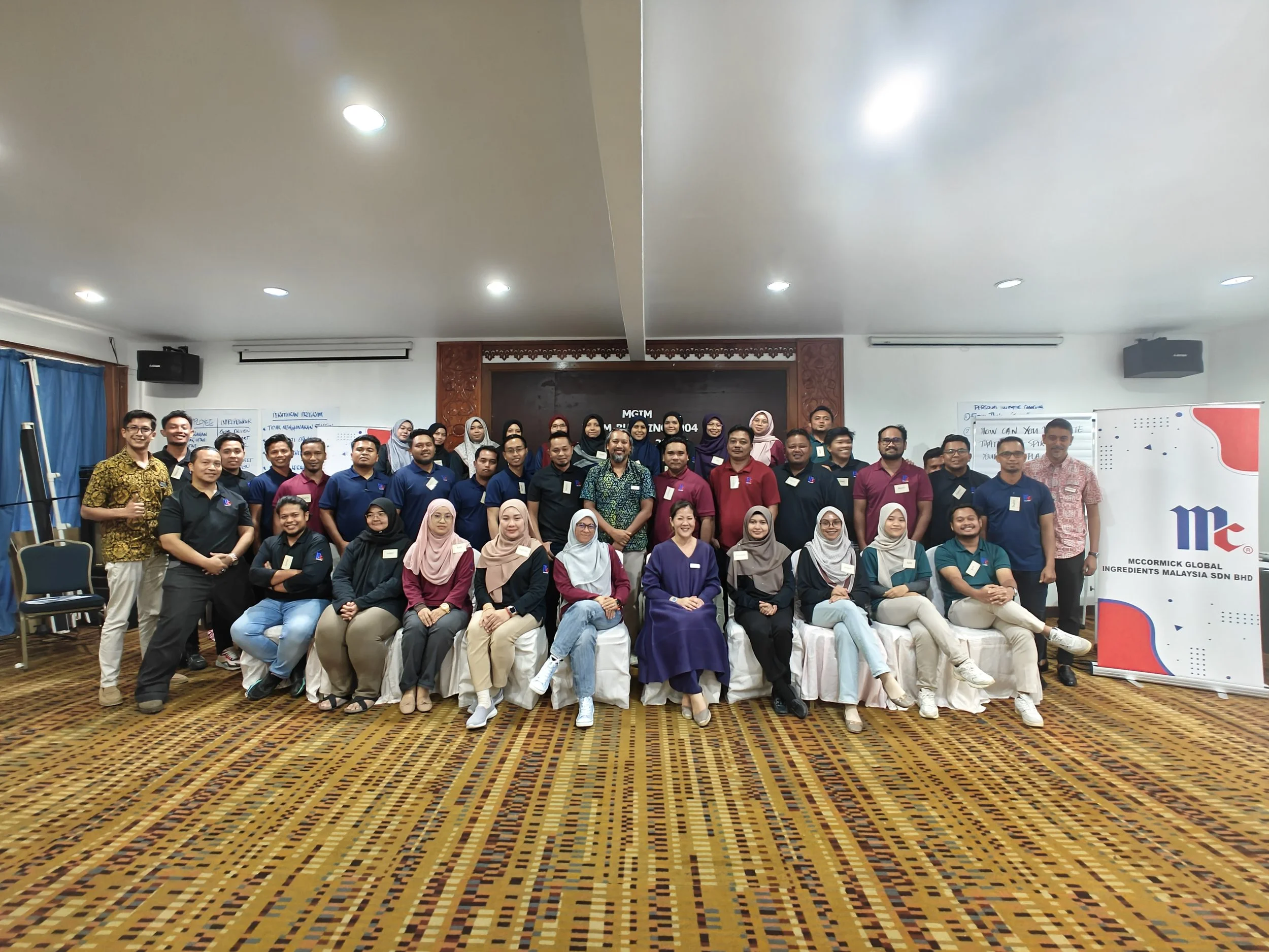 Group photo of people attending a seminar or training workshop in a conference room with whiteboards and a banner.