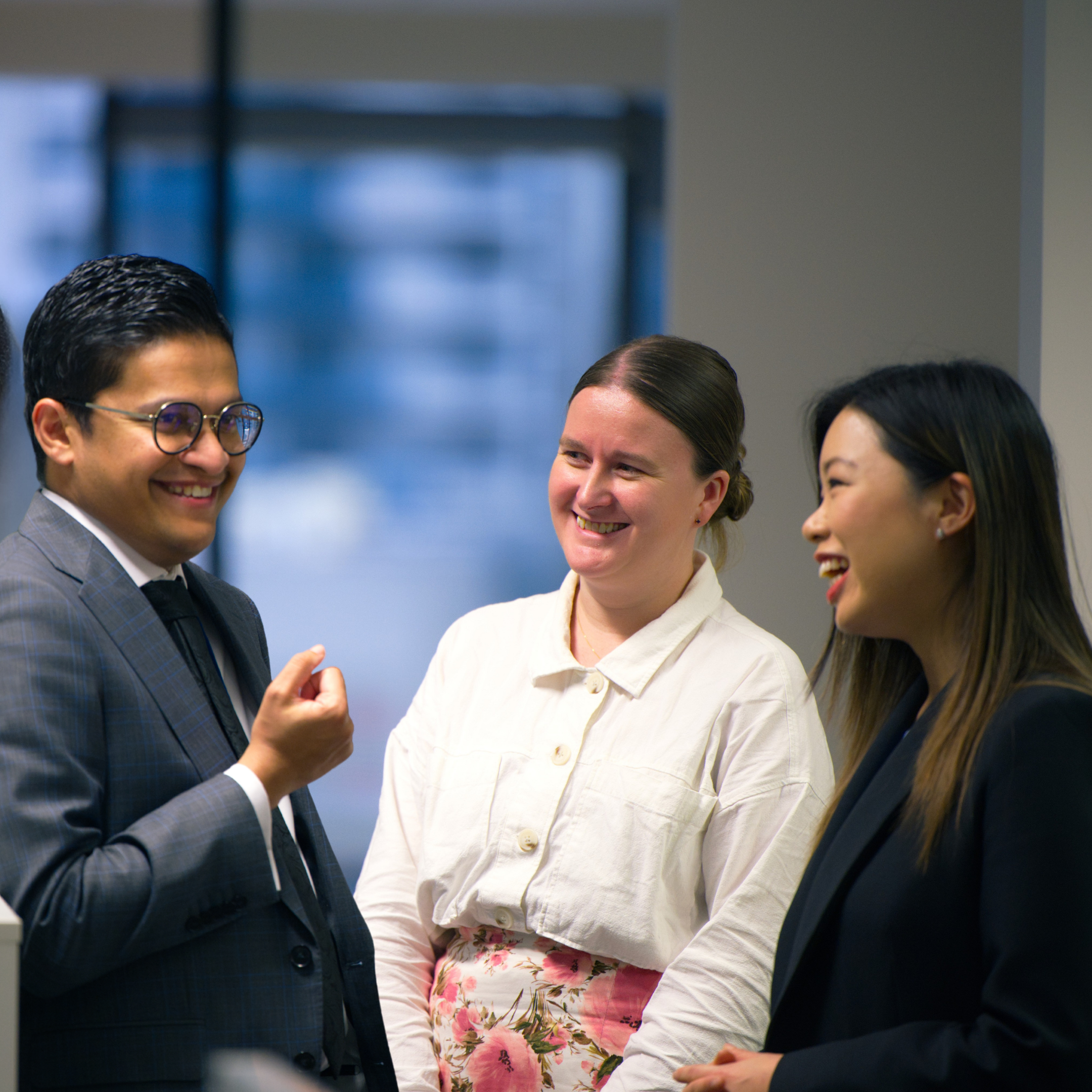 Three diverse professionals, two women and one man, engaged in a cheerful conversation in an office setting.
