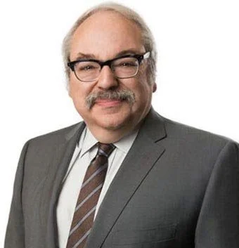 A middle-aged man with glasses and a mustache wearing a gray suit, white shirt, and striped tie, smiling at the camera.