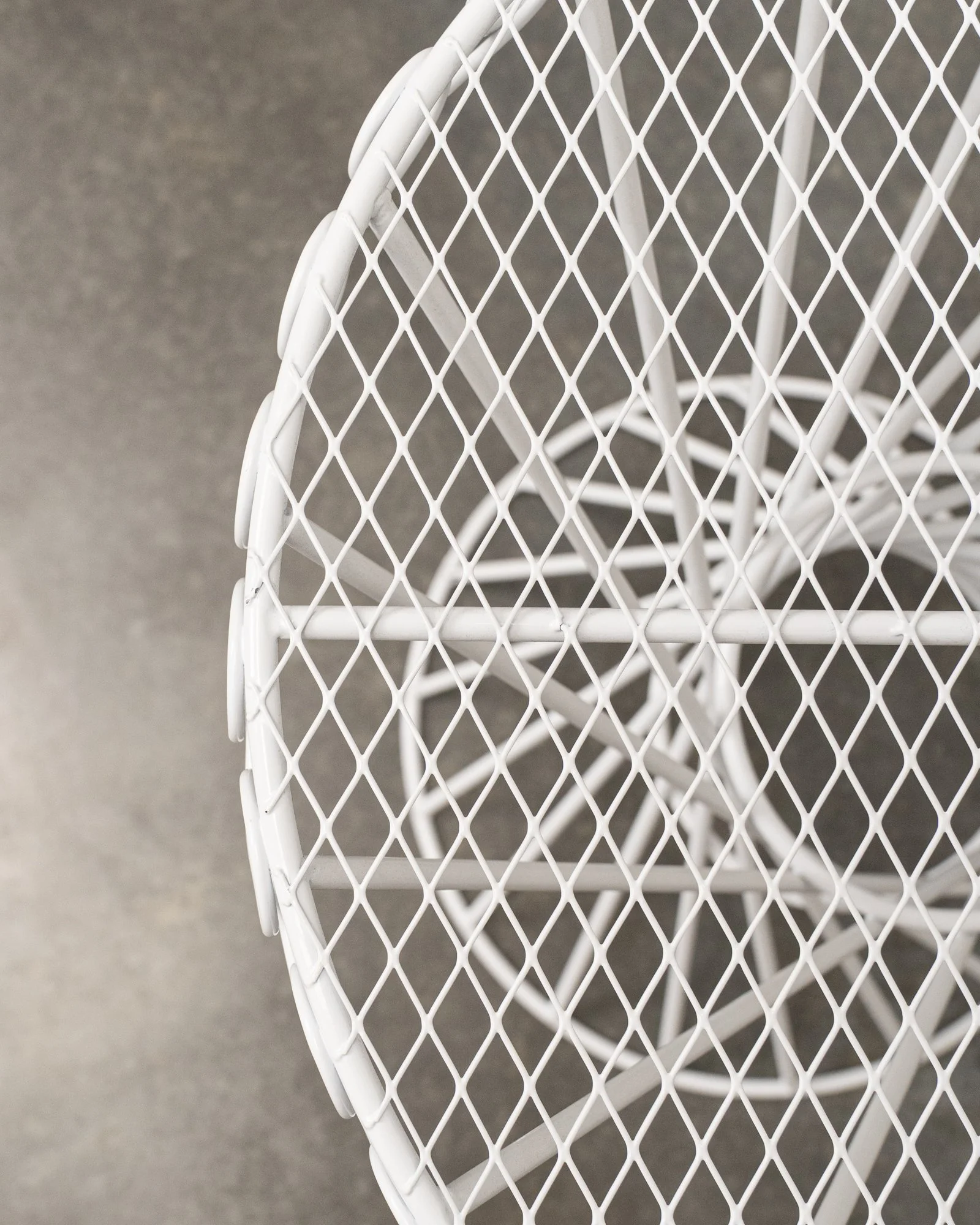 Close-up of a white metal wire mesh table top and a part of the chair with a grey background.