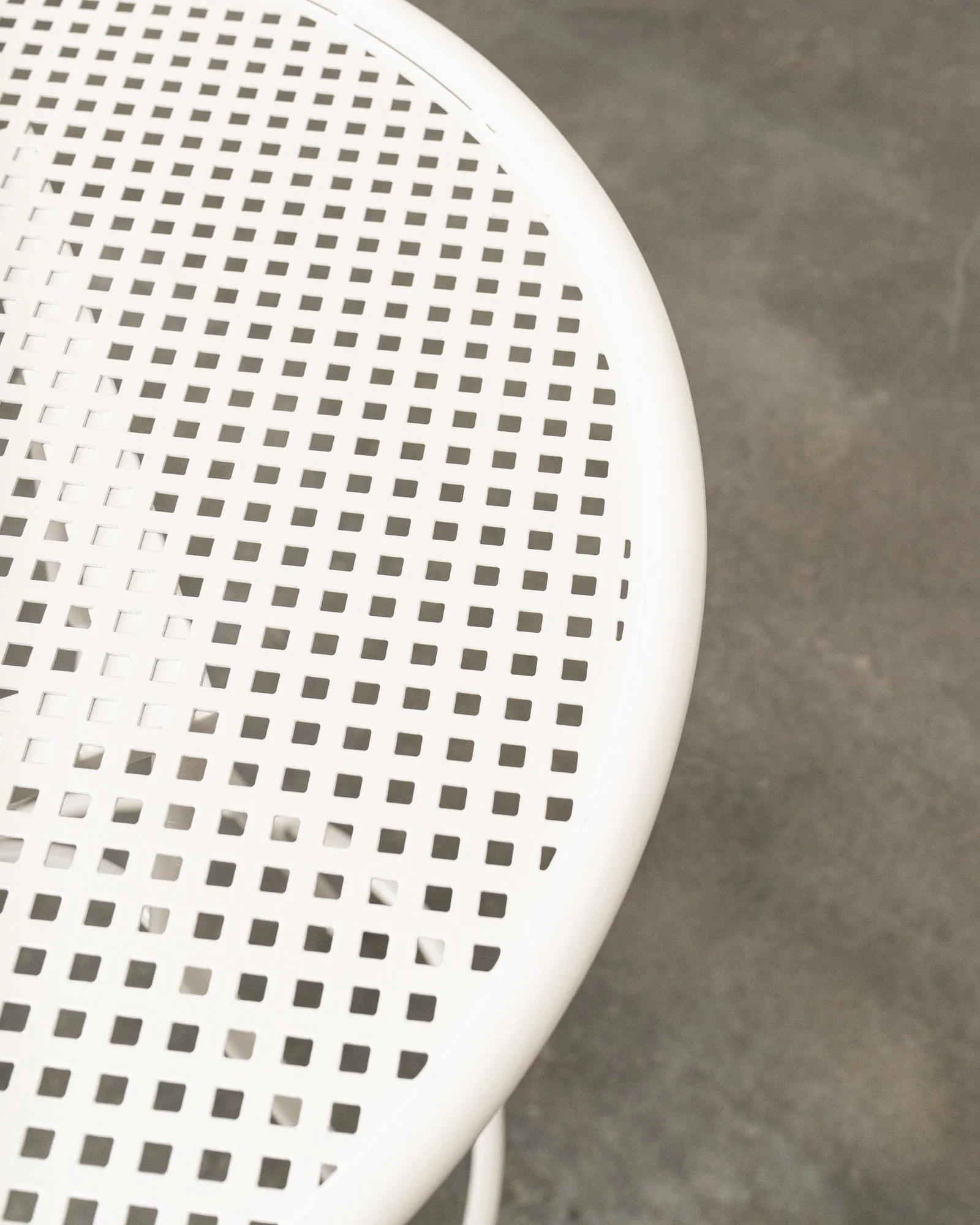 Close-up of a white, perforated plastic chair with a gray, textured floor in the background.