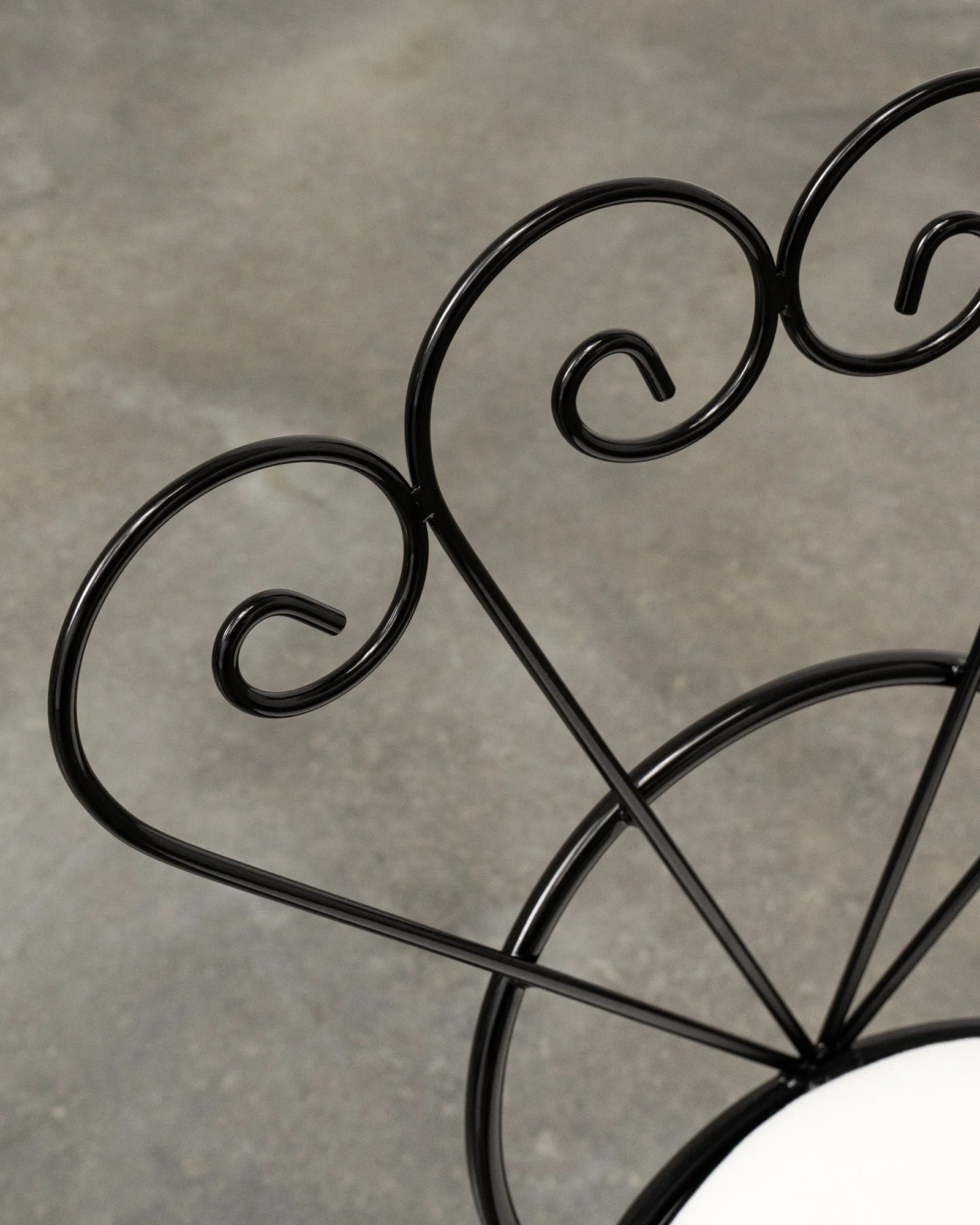Close-up of black metal decorative scrollwork, part of furniture or decorative item, against a gray background.