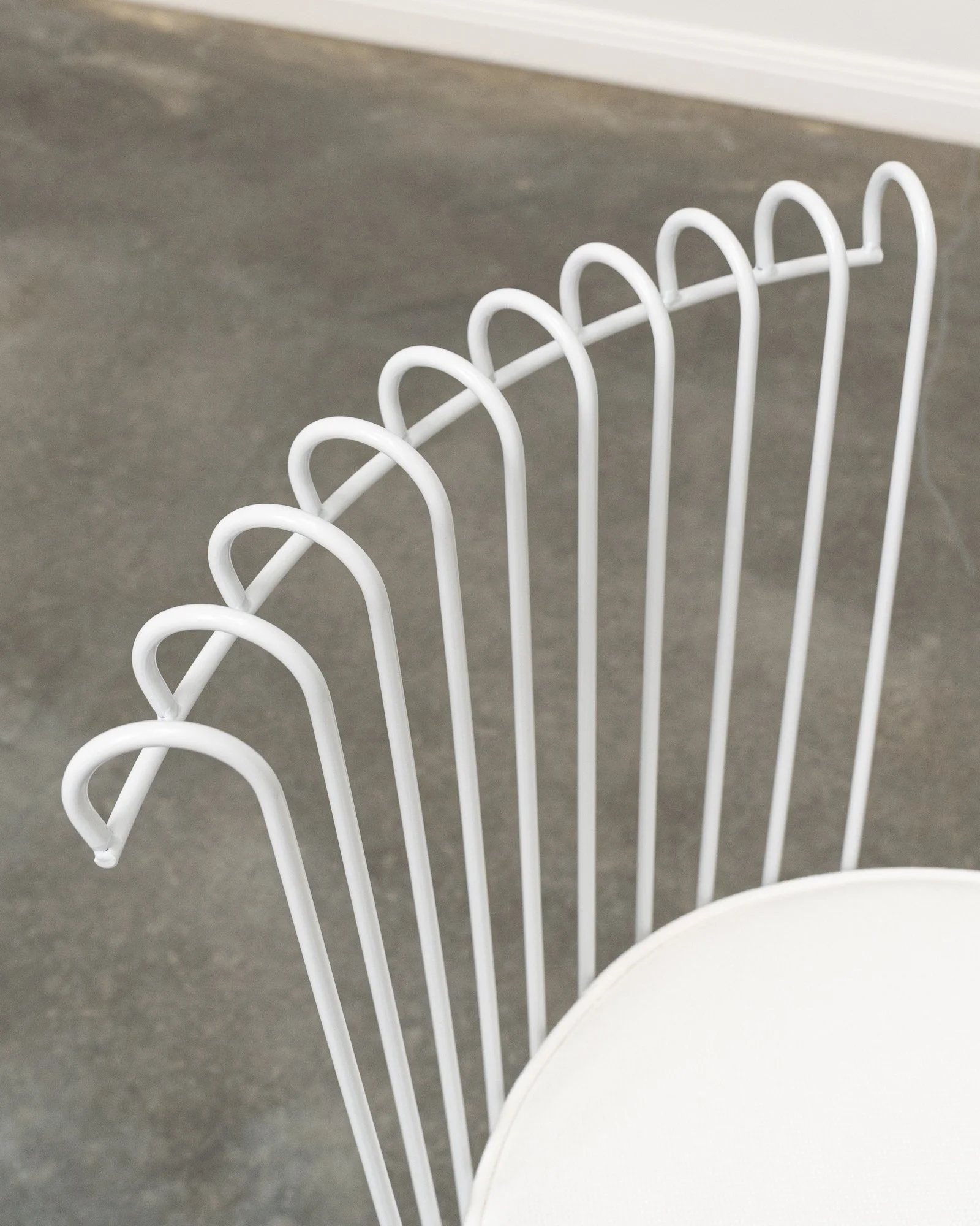 Close-up of a white wire rack with a curved handle on a gray floor, with a white wall and baseboard in the background.