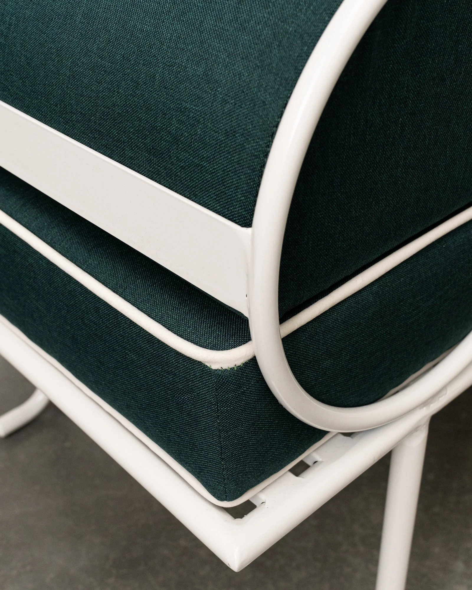 Close-up of a white metal-framed chair with dark teal fabric seat and backrest, on a dark floor.