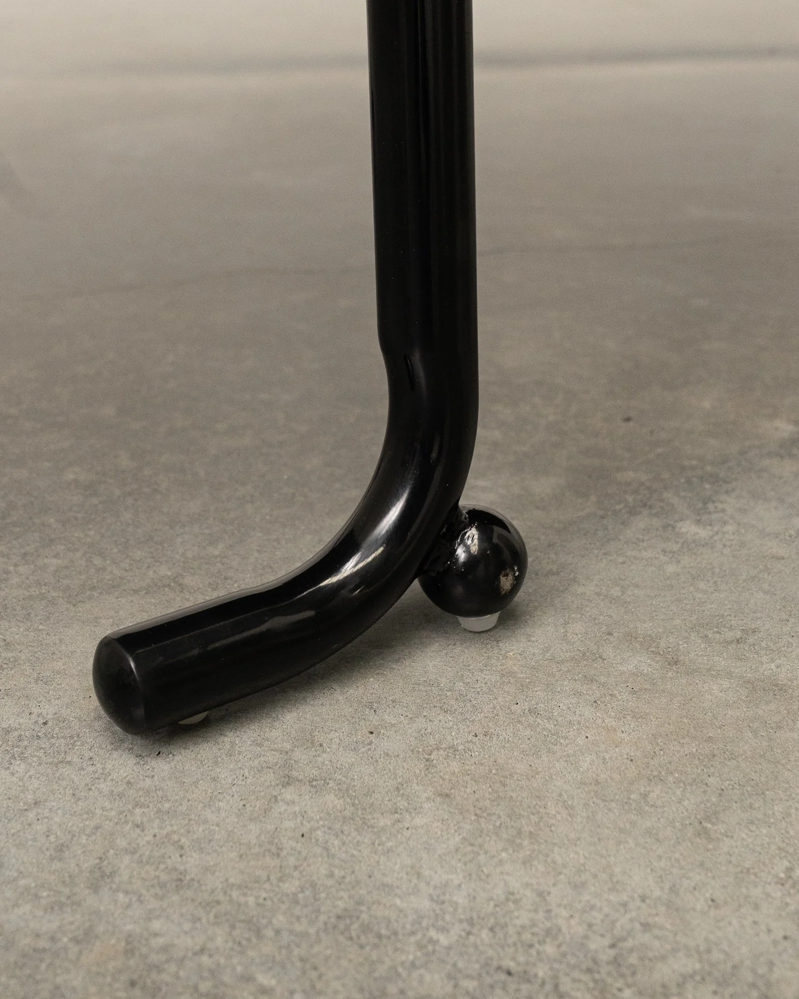 Close-up of a black metal hook or stand with a small spherical foot on a gray surface.
