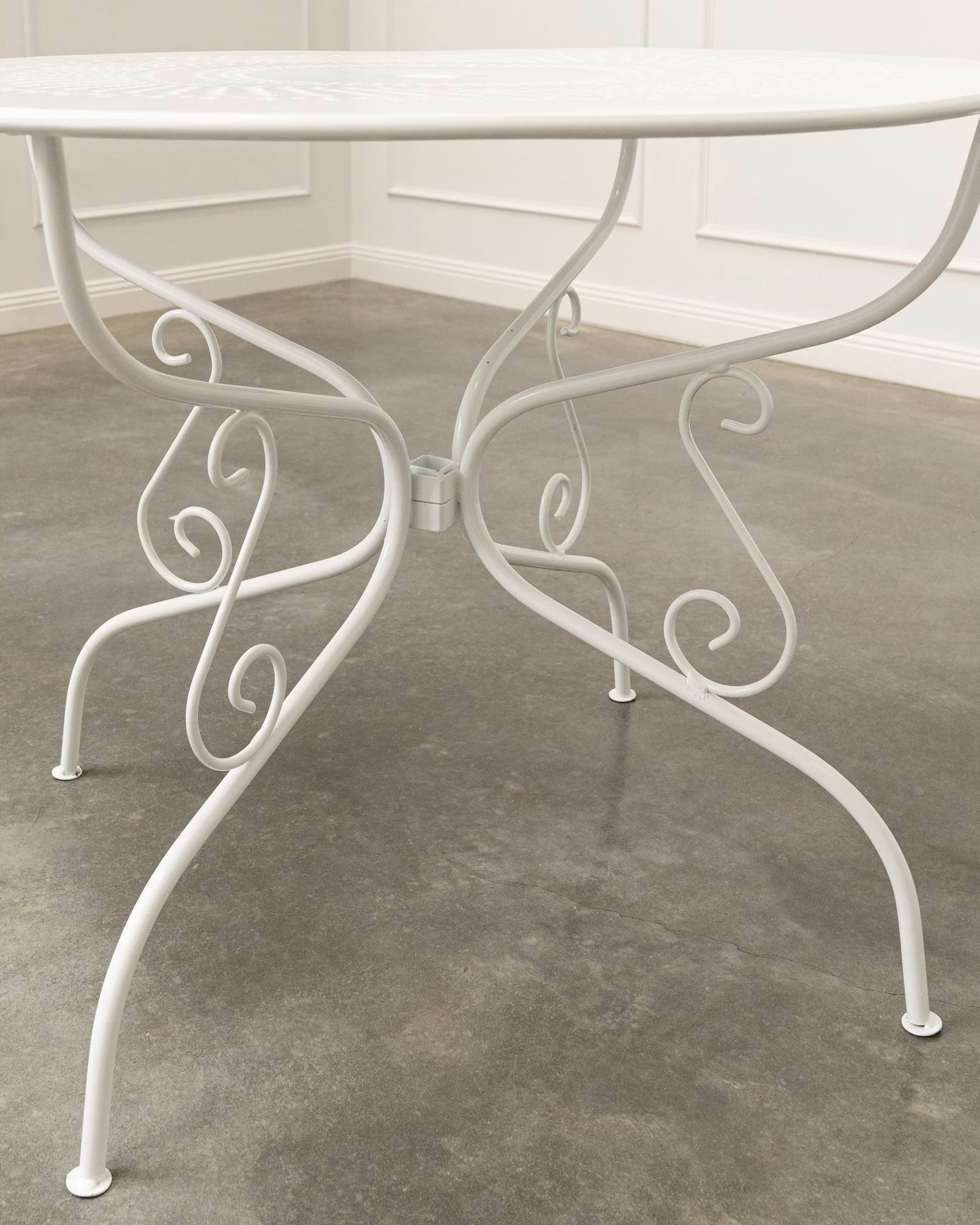 White metal table with decorative scrollwork legs in a room with white walls and gray flooring.
