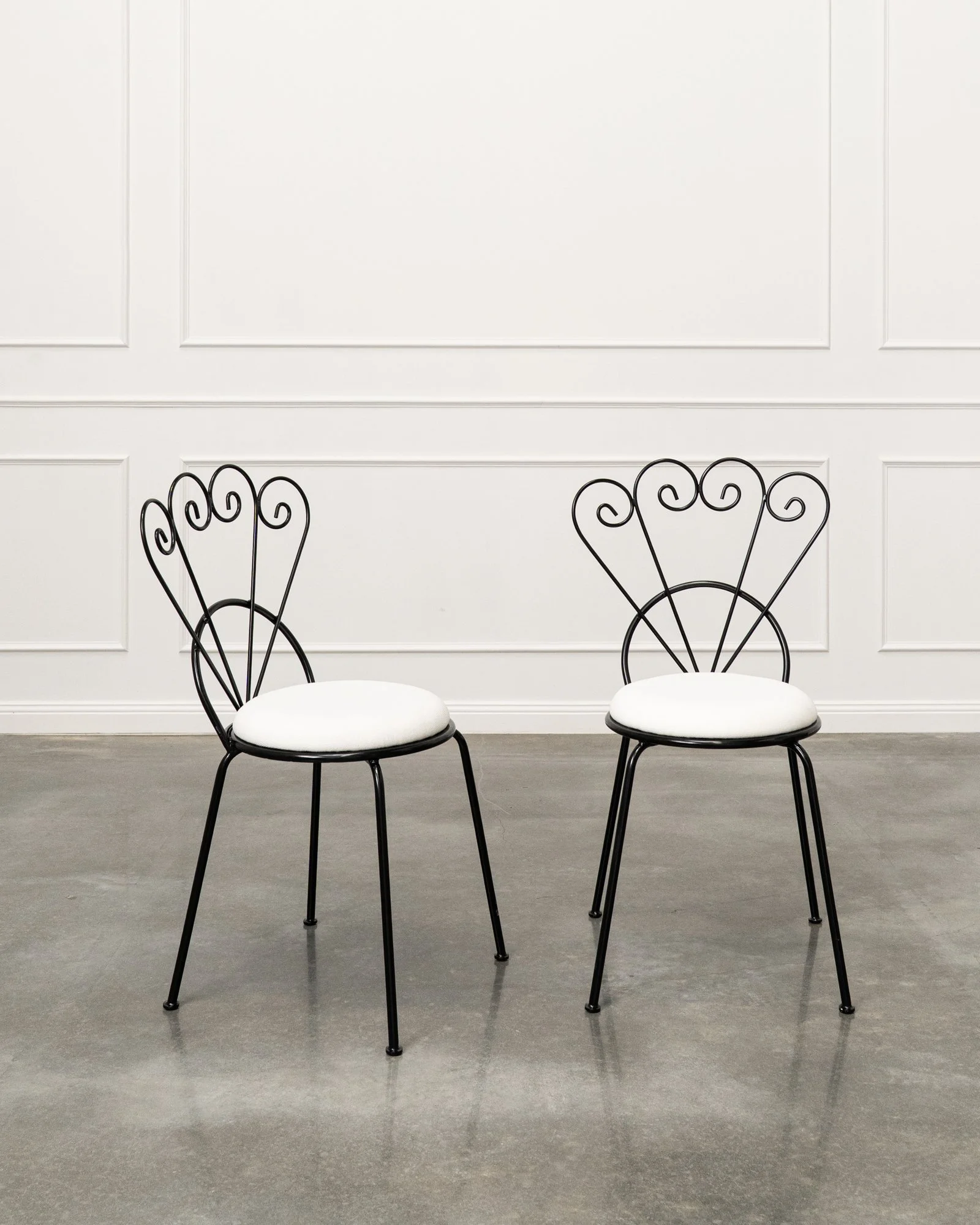 Two black metal chairs with white cushioned seats in front of a white paneled wall.