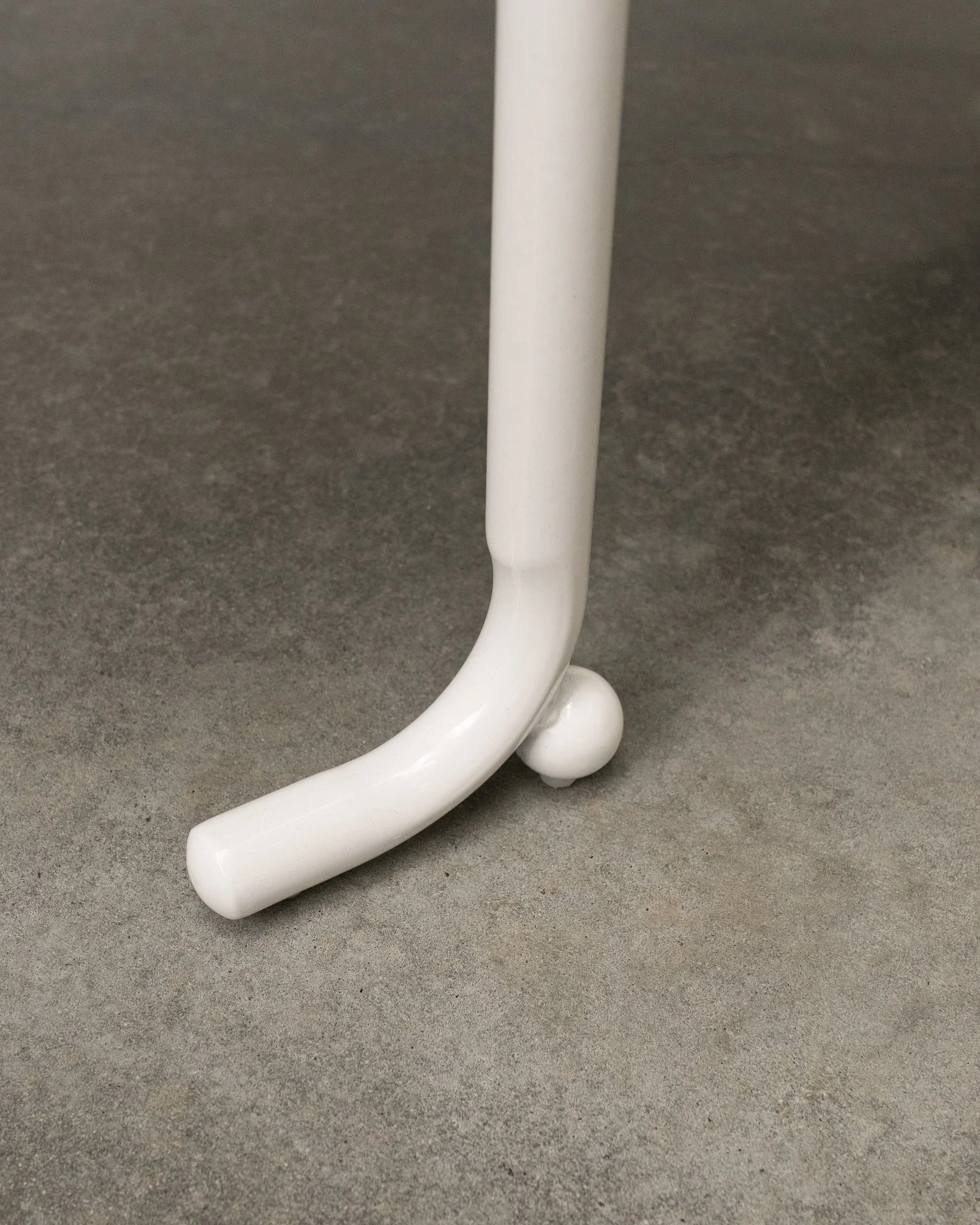 Close-up of a white curved metal leg with a ball at the end, set on a gray surface.