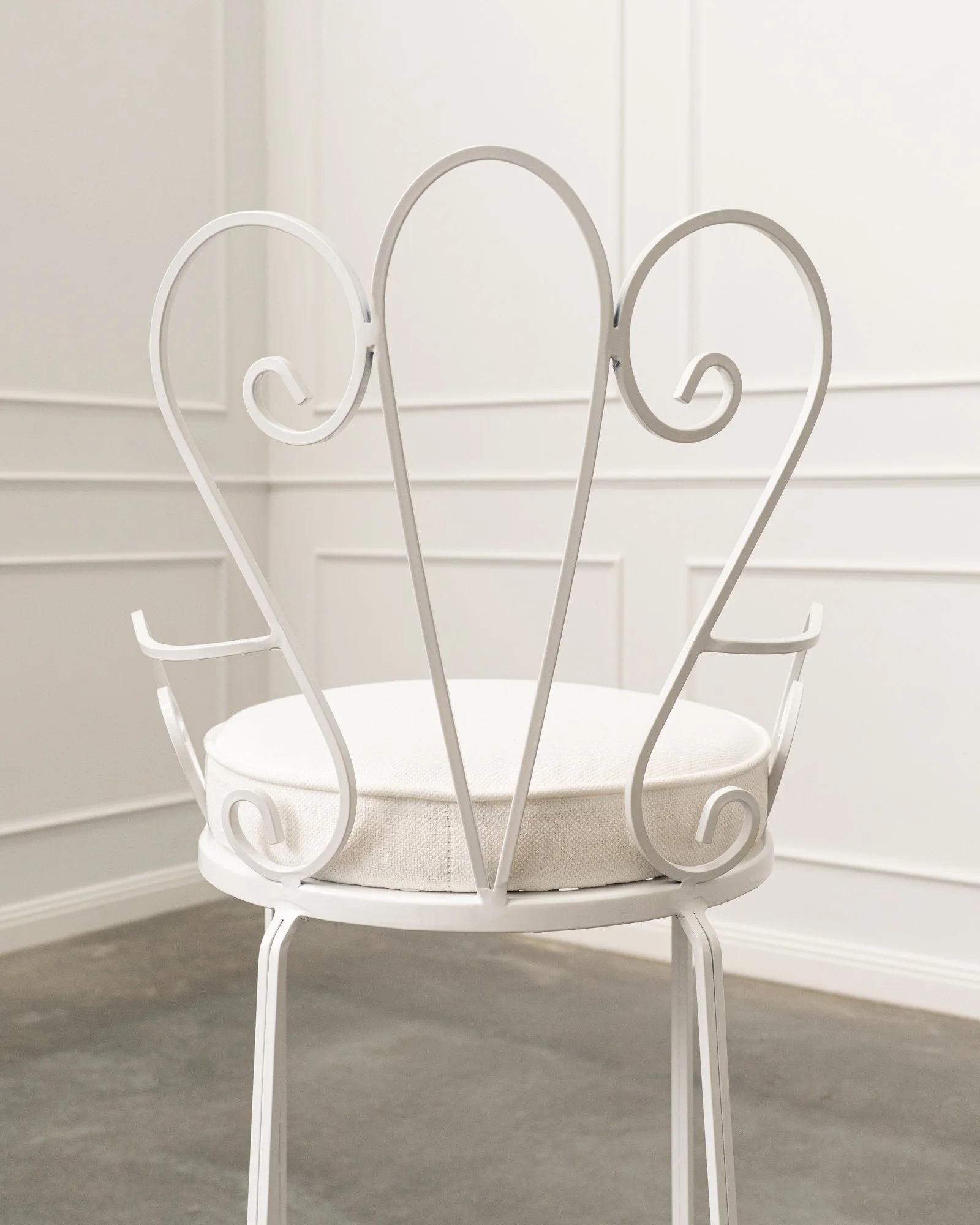 A white metal chair with ornate scrollwork in a bright room with white walls and gray carpet.