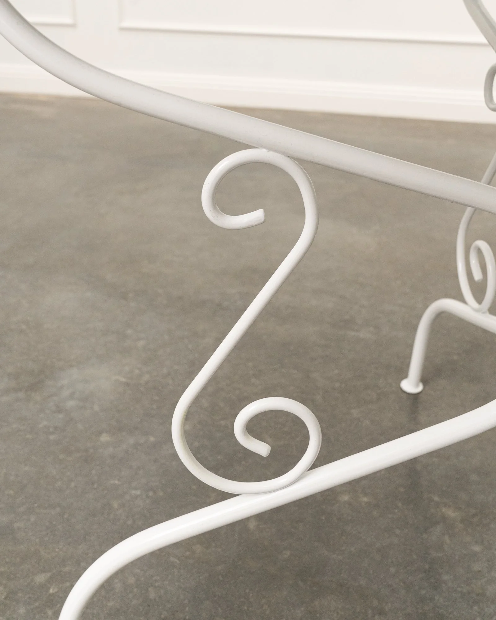 Close-up of a white, decorative metal structure with curled and swirling design elements, set against a neutral gray background.