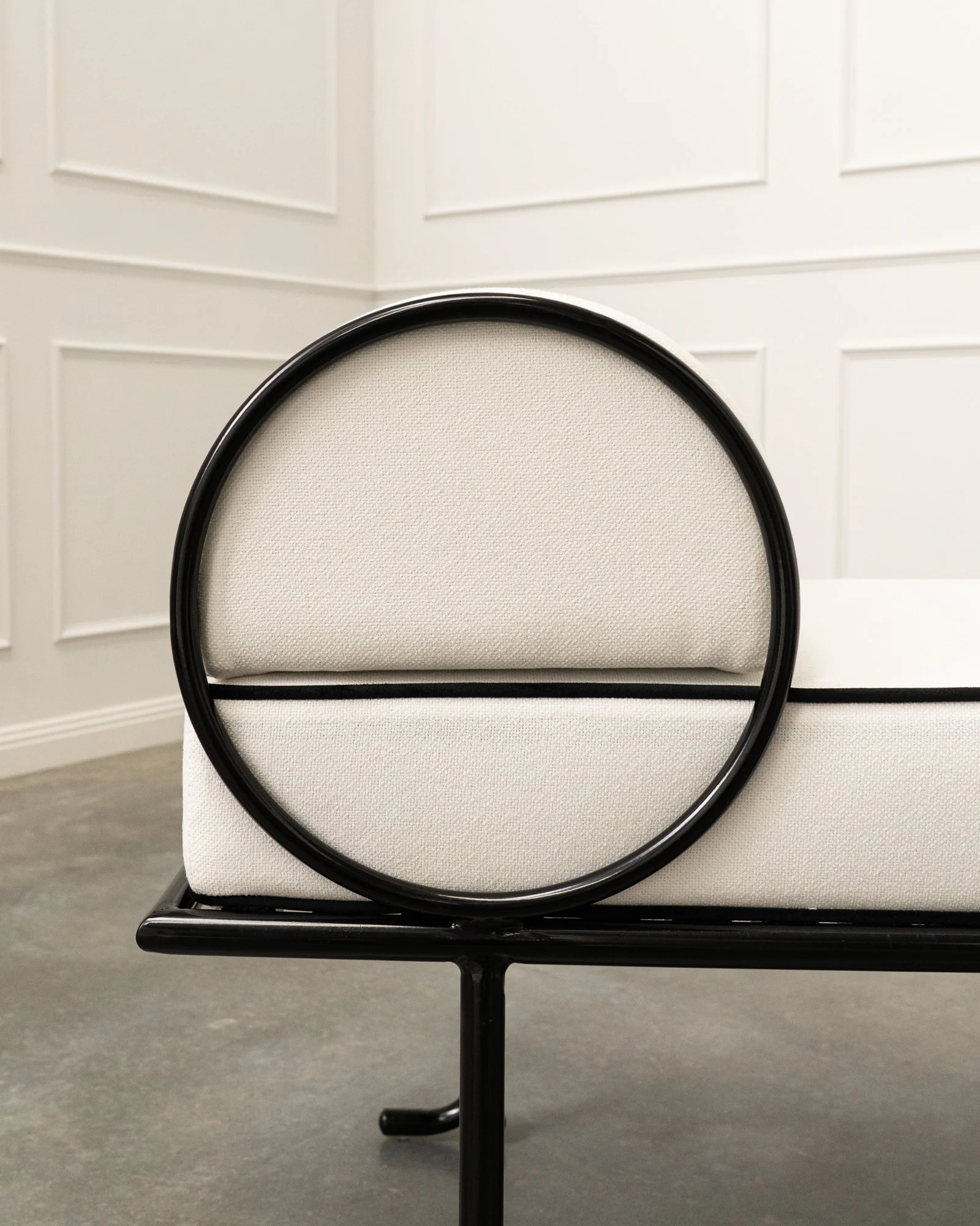 Close-up of a white chair with a black frame, positioned on a gray floor against a white paneled wall.