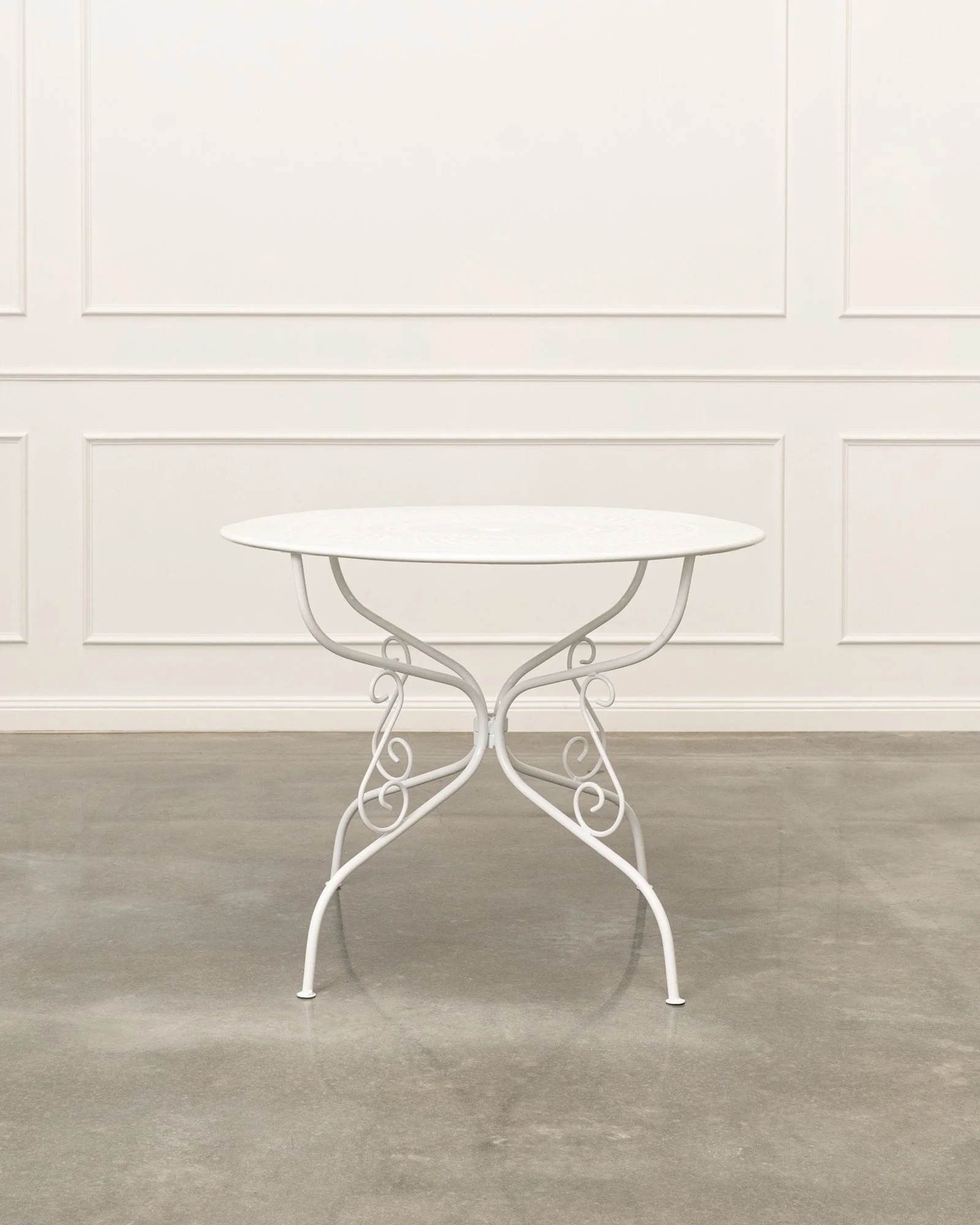 White round table with ornate metal legs against a white paneled wall.