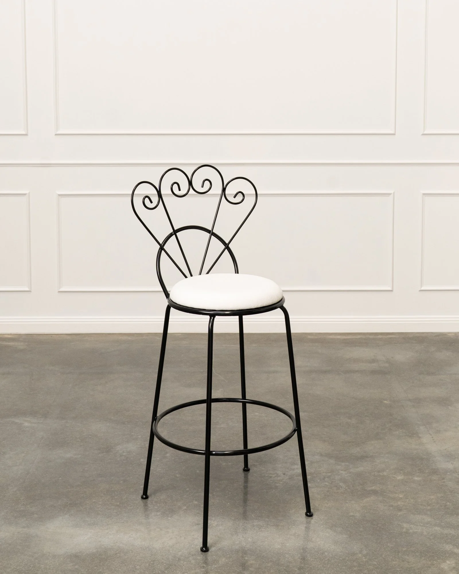 A black metal chair with a white cushioned seat in front of a white paneled wall.