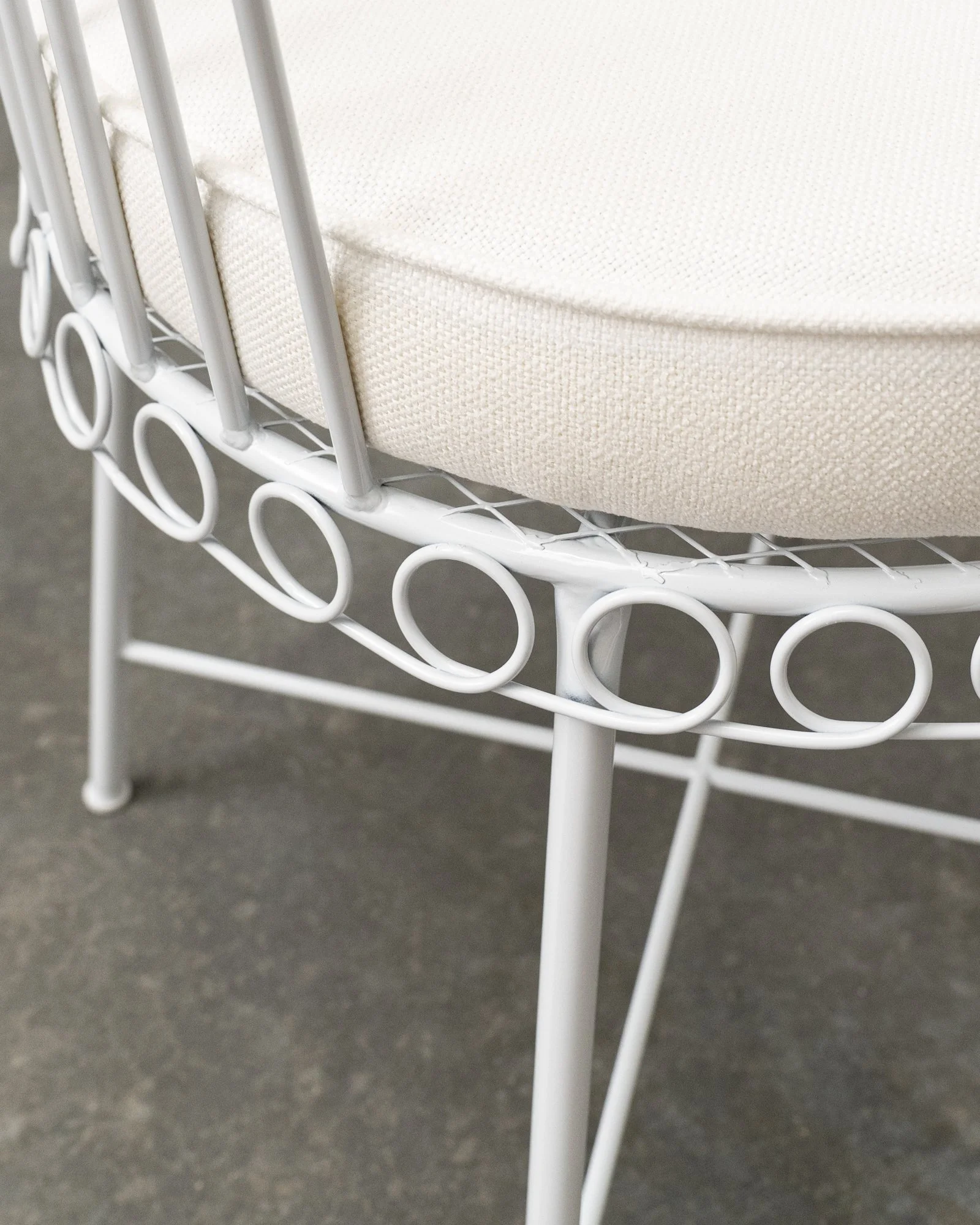 Close-up of white metal chair with a curved, circular design on the frame, set on a gray surface.