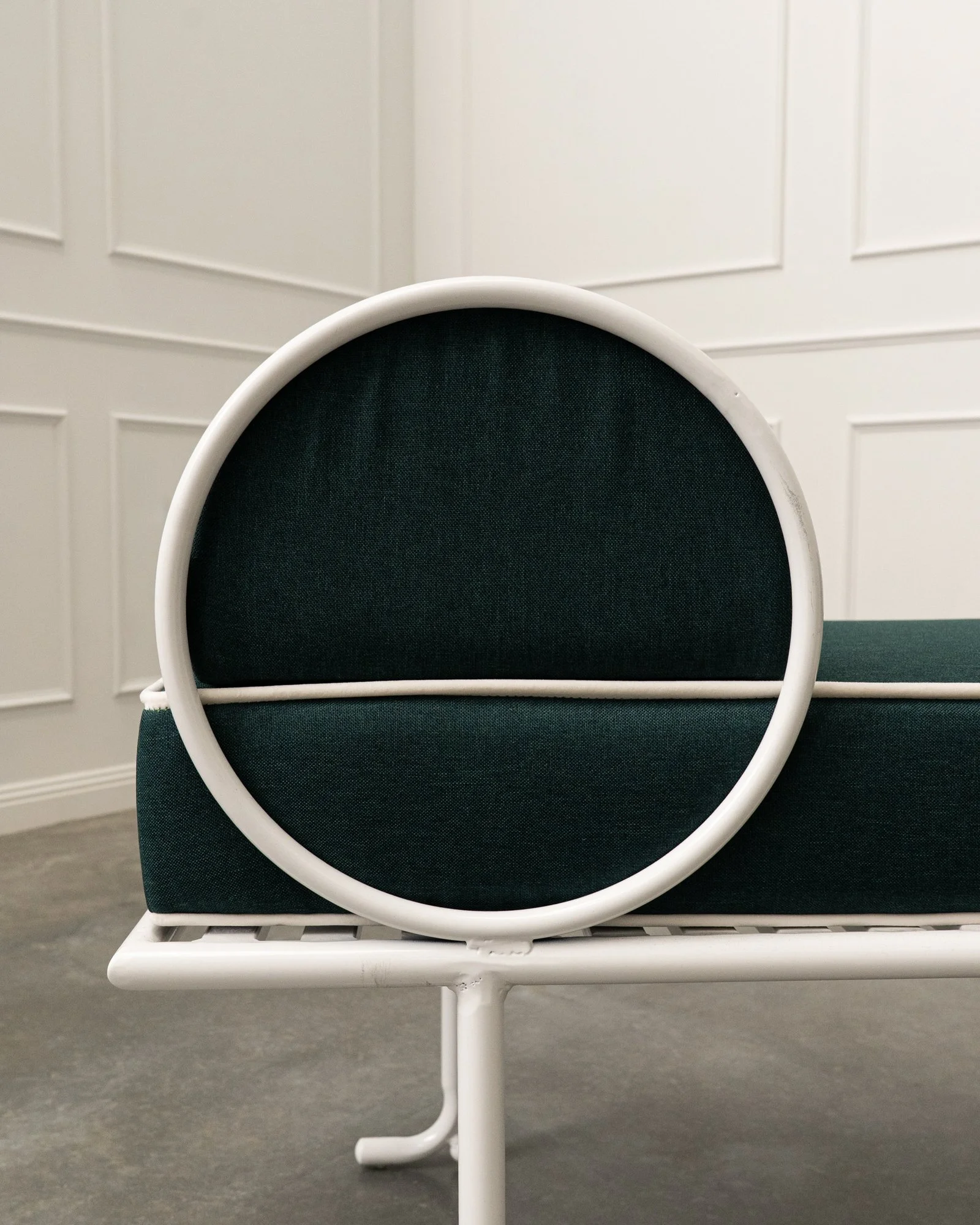 Close-up of a white metal chair with a black cushion in front of a white paneled wall.