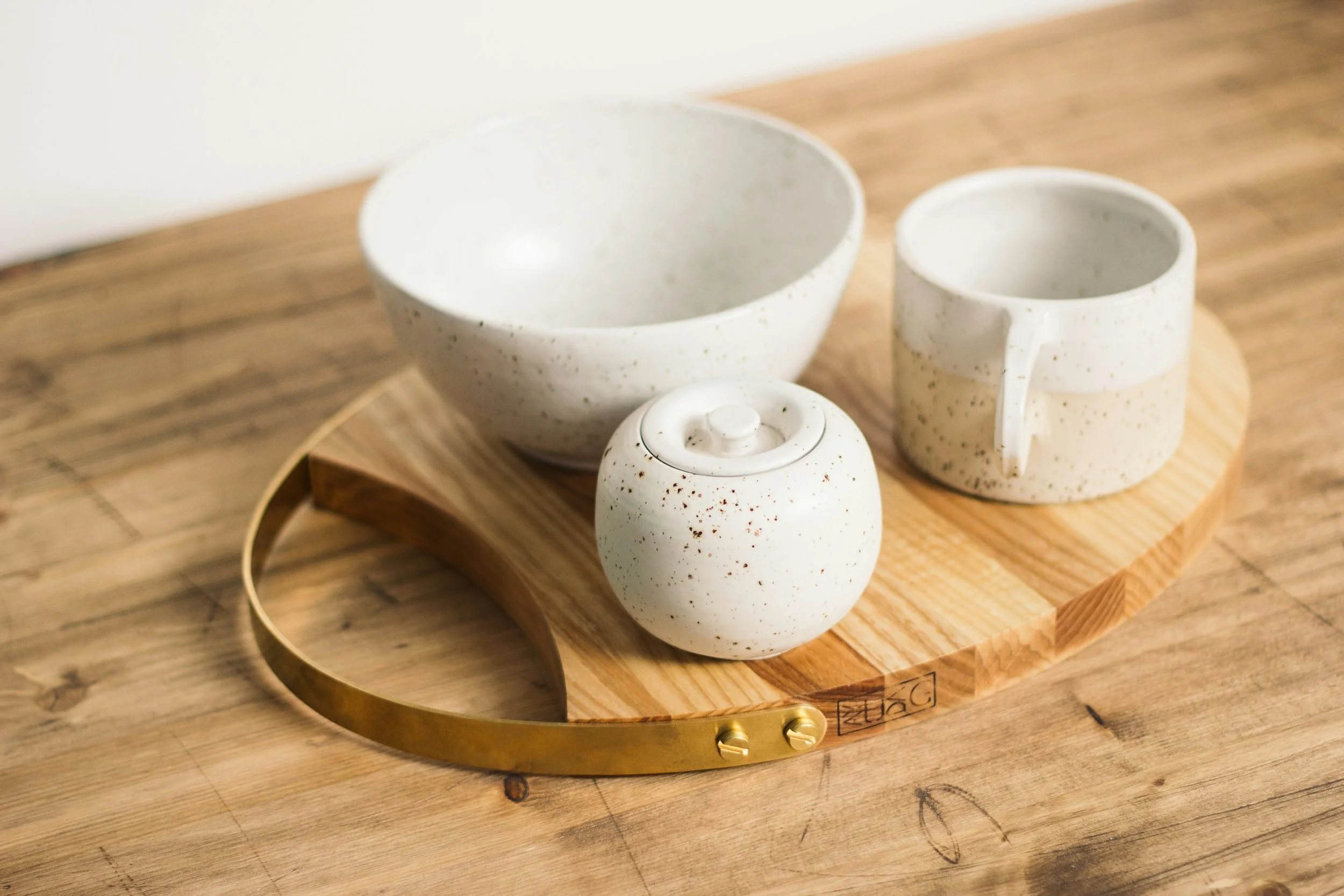 Ceramic bowls, mug, and a sugar bowl with lid on a wooden tray, placed on a wooden surface.