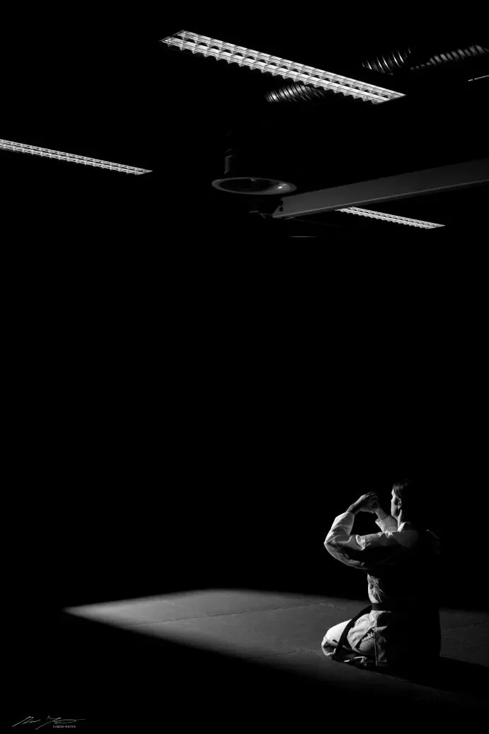 Henkilö polvistuneena tatamille. Tumma kuva.