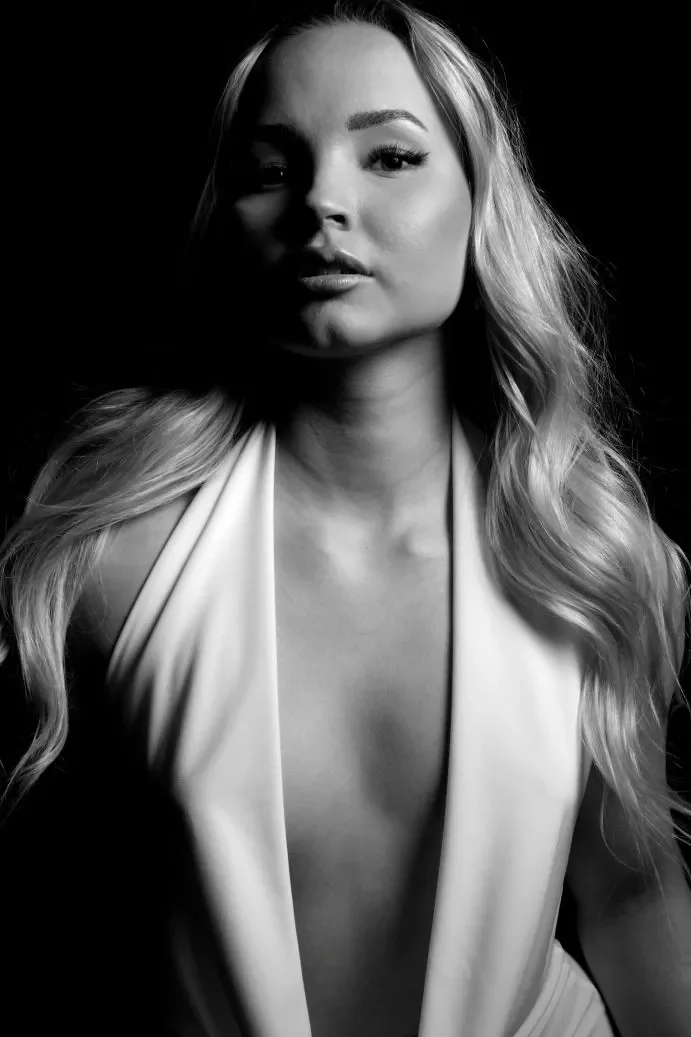 Nuori nainen mekko päällä, vaaleat hiukset kihartuneena kasvojen sivuilla.  Harmaasävyinen kuva, musta tausta.