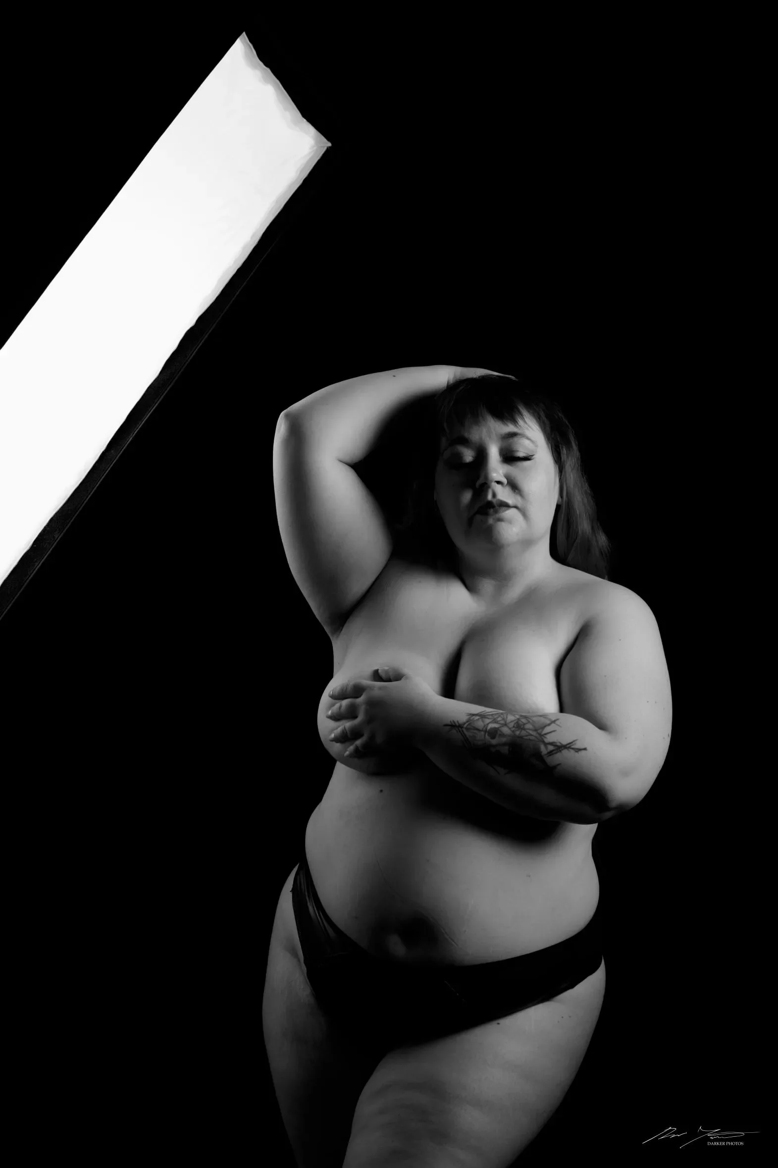 Harmaasävyinen kuva, jossa nainen poseeraa käsi pään päälle taivutettuna.