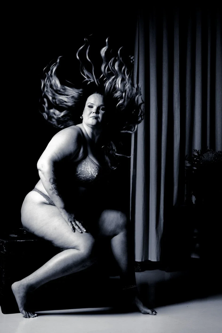 Tummasävyinen kuva naisesta, joka istuu ja katsoo sivulle. Kuvassa on varjoja ja valoja.