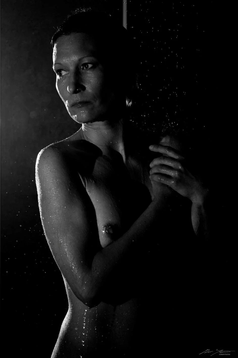 Mustavalkoinen kuva naisesta, joka seisoo tummassa ympäristössä.