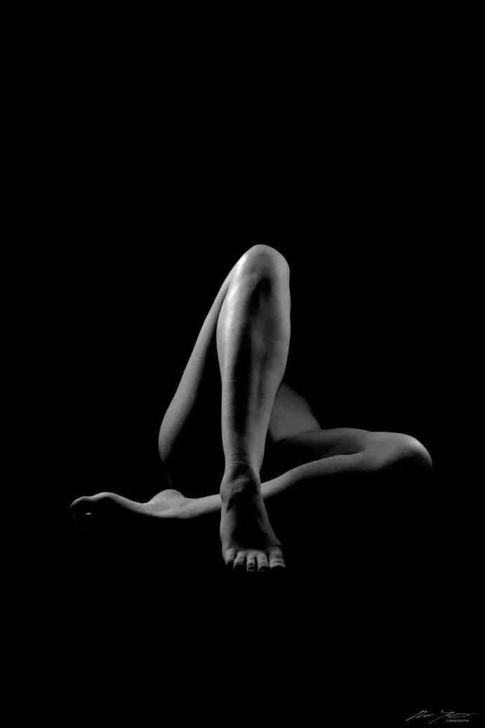 Tumma kuva, hieman valoa tulee ihmisen jalkojen päälle. Toinen jalka koukussa ja toinen sivulle taivutettuna.