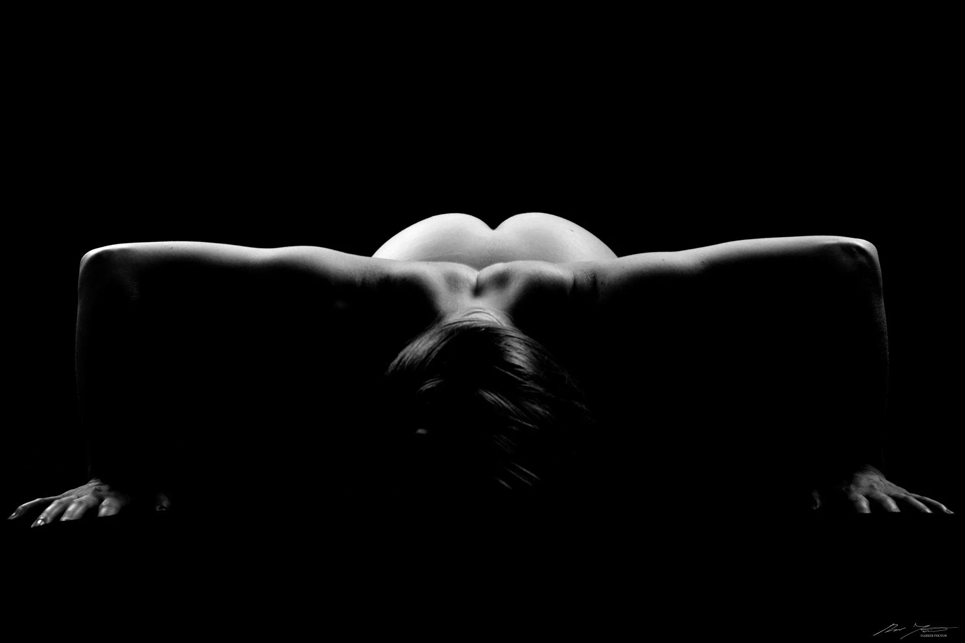 Tummasävyinen kuva henkilön selästä ja käsivarsista. Kuvassa on varjoja ja valoja.