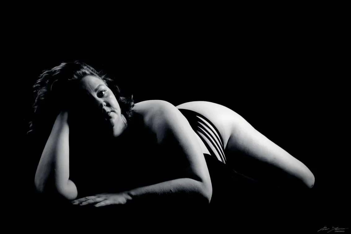 Mustavalkoinen valokuva naisesta makaamassa kyljellään, nojaten toiseen käteensä.