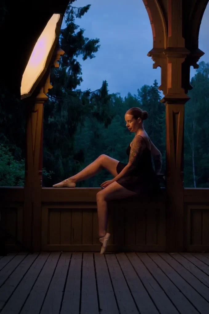 Nainen istuu rakennuksen kaiteella puistossa, taustalla puuta ja taivasta.