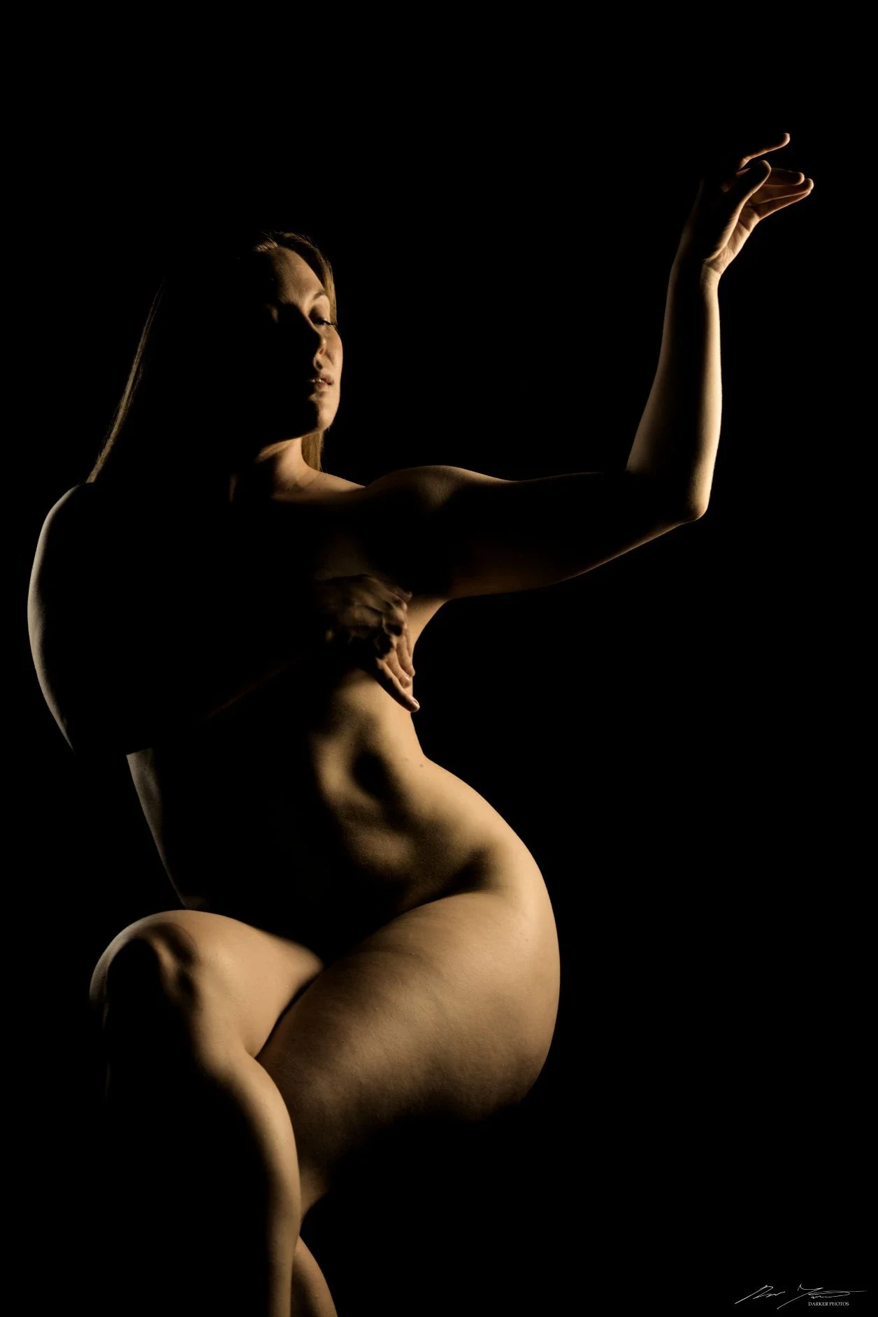 Valokuva naisesta, joka poseeraa tummasävyisessä kuvassa. Valot ja varjot näkyvät naisen vartalolla.
