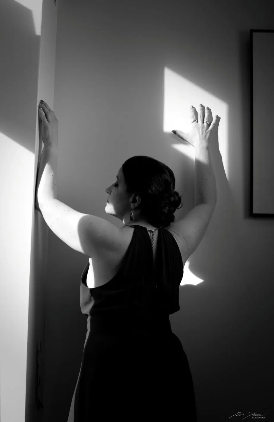 Mustavalkokuva naisesta, joka seisoo seinää vasten ja koskettaa sitä käsillään.