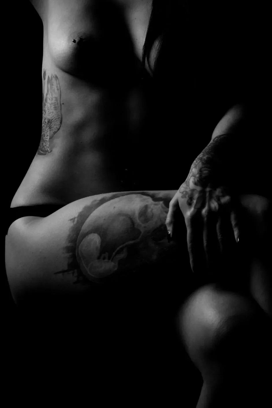 Mustavalkoinen kuva, jossa näkyy naisen vartaloa, jolla on tatuointeja.