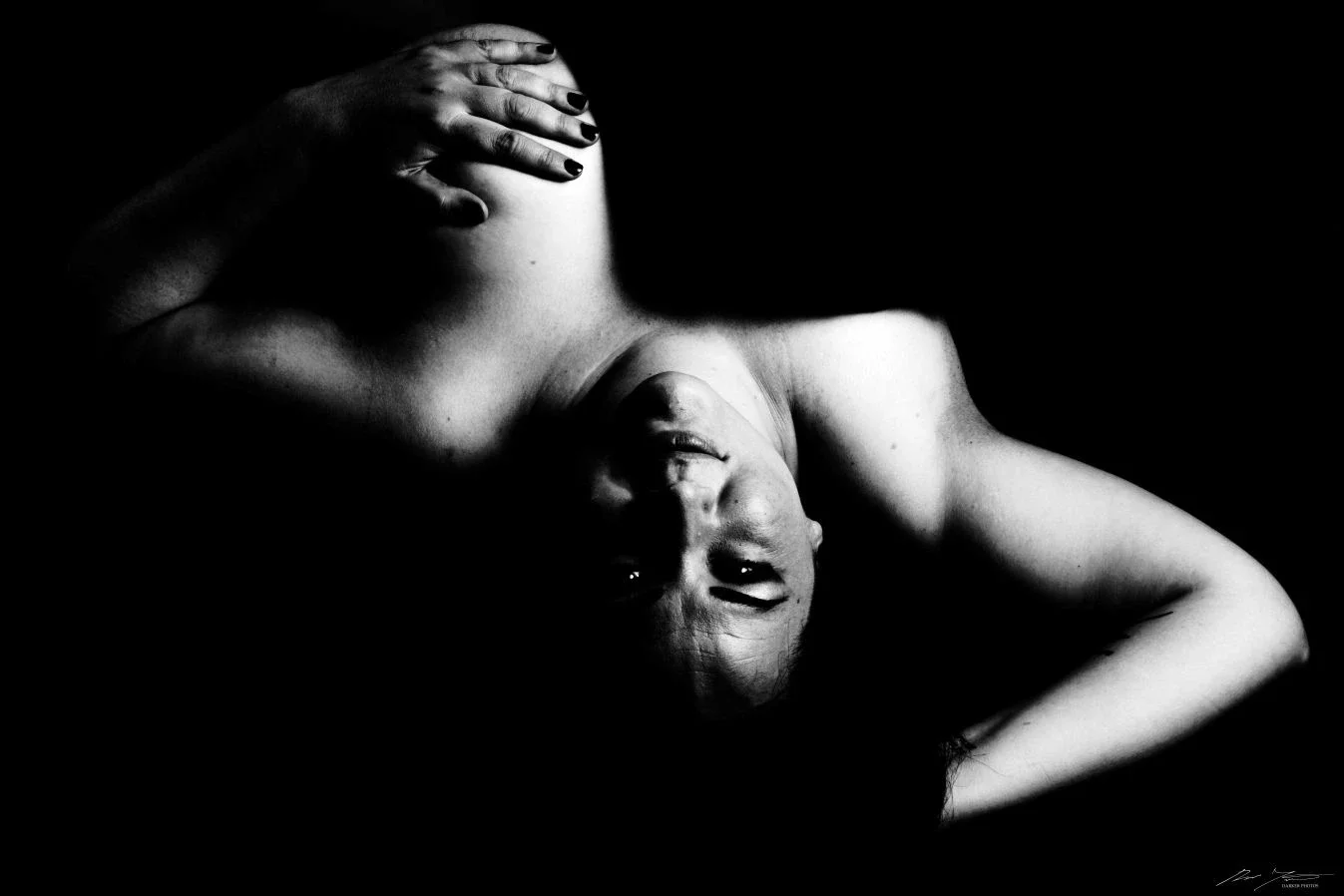 Mustavalkoinen kuva naisesta makuuasennossa, käsi pään päällä, katse suoraan kameraan.