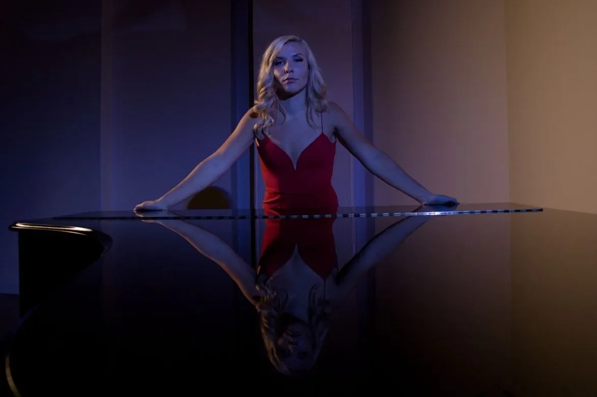 Nainen punaisessa mekossa seisoo flyygelin takana.