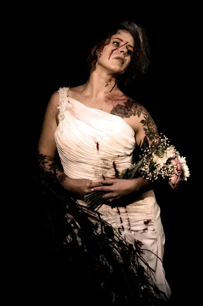 Nainen, joka on pukeutunut valkoiseen mekkoon. Tumma tausta, naisen ylle tulee valoa.